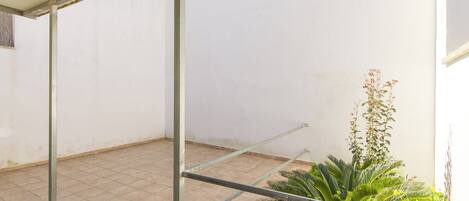 Un patio cubierto con suelo de baldosas, vigas de metal y plantas verdes.