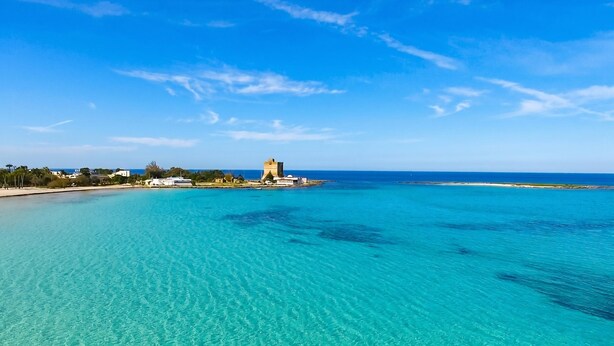 A coastal view with clear turquoise waters, a distant castle-like structure, and a clear sky. - Casa Lory 3 cozy and near the sea (Nardò)