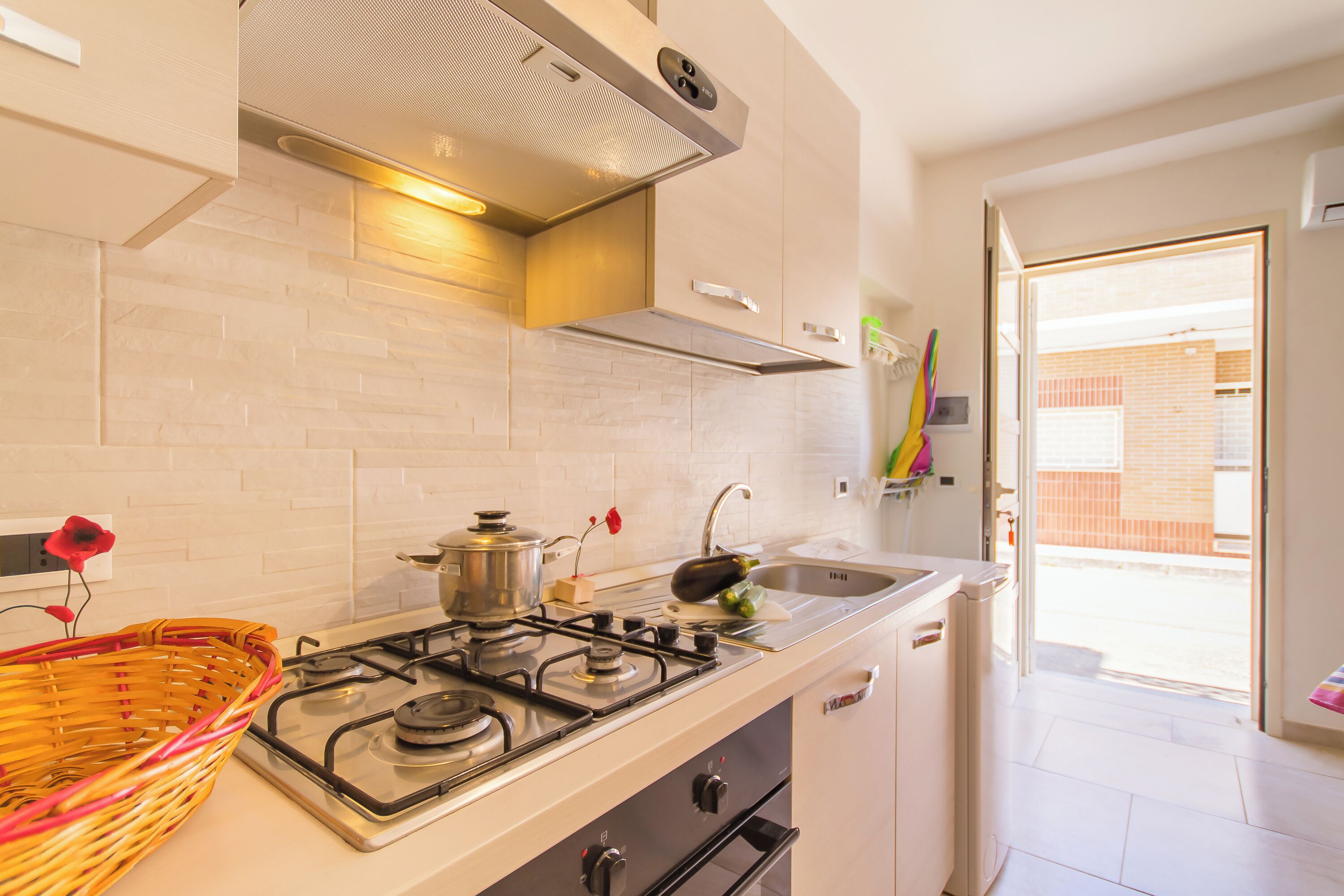 A modern kitchen with a gas stove, a sink, and a window leading to a balcony.