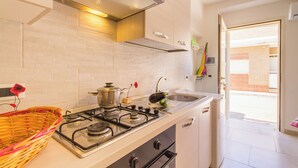 A modern kitchen with a gas stove, a sink, and a window leading to a balcony. - Casa Lory 3 cozy and near the sea (Nardò)