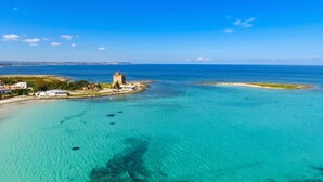 An aerial view of a coastal area with clear turquoise waters, a prominent tower, and a small island with a sandy beach. - Casa Lory 3 cozy and near the sea (Nardò)