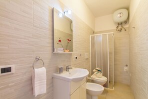 A modern bathroom with a white sink, mirror, and toilet, a towel rack, and a shower area.