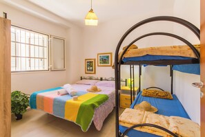 A room with a bunk bed, a single bed, a window with bars, a hanging light fixture, and a small plant.