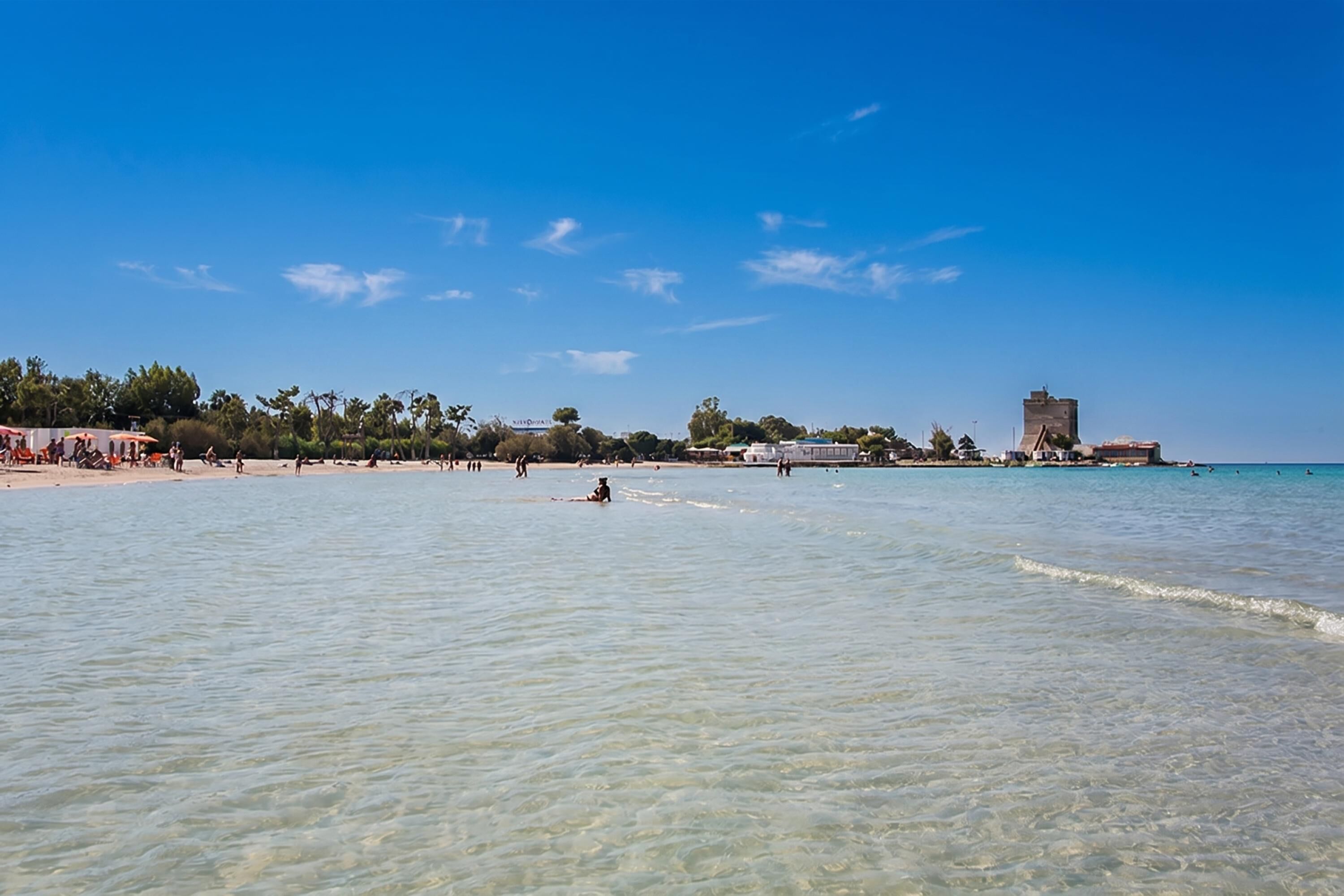 Une plage à l’eau claire, avec quelques personnes et, au loin, une structure qui ressemble à un château.