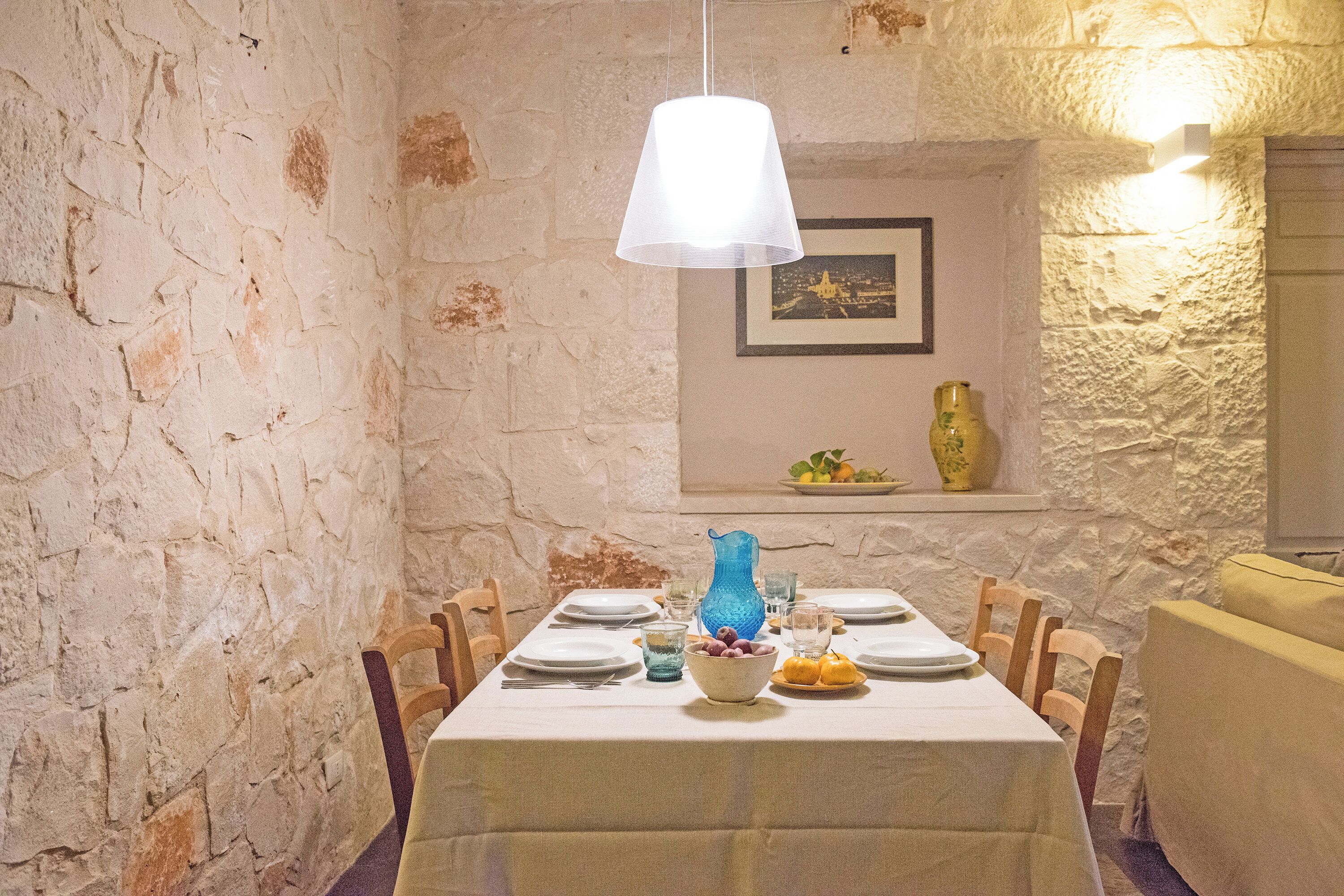 A dining table set with plates, glasses, and a vase, in a room with stone walls and a hanging light fixture.