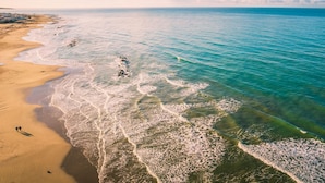 Ein Luftbild zeigt einen Strand mit klarem türkisblauem Wasser und einem sandigen Ufer.