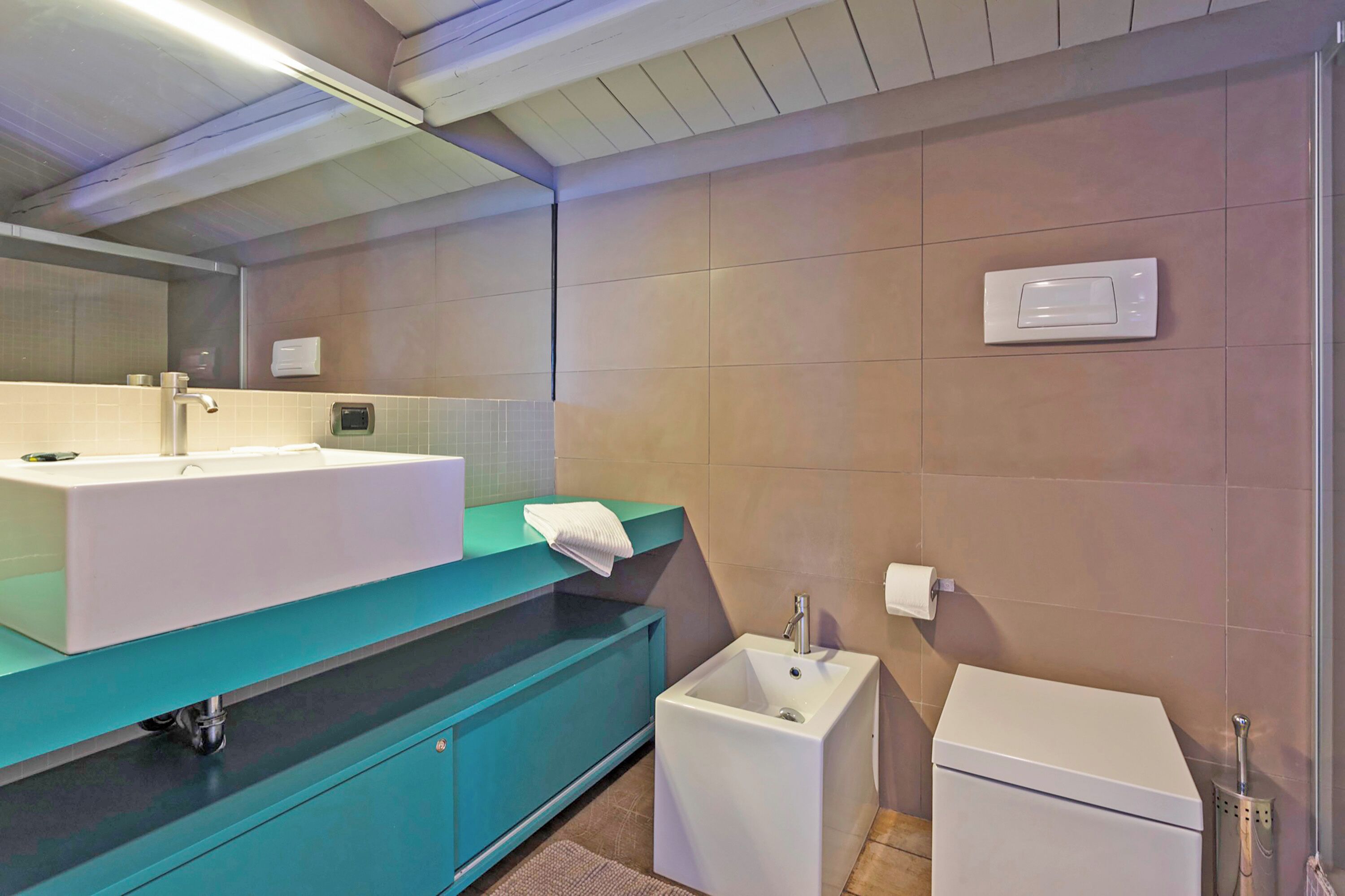 A modern bathroom with a large white sink, a smaller sink, a mirror, and a toilet.