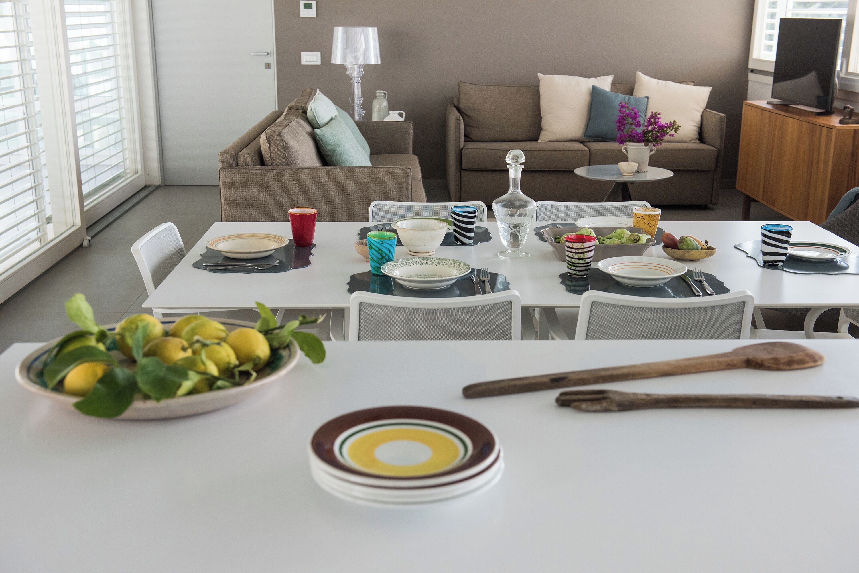 A dining area with a table set for four, a bowl of lemons, and a television in the background.