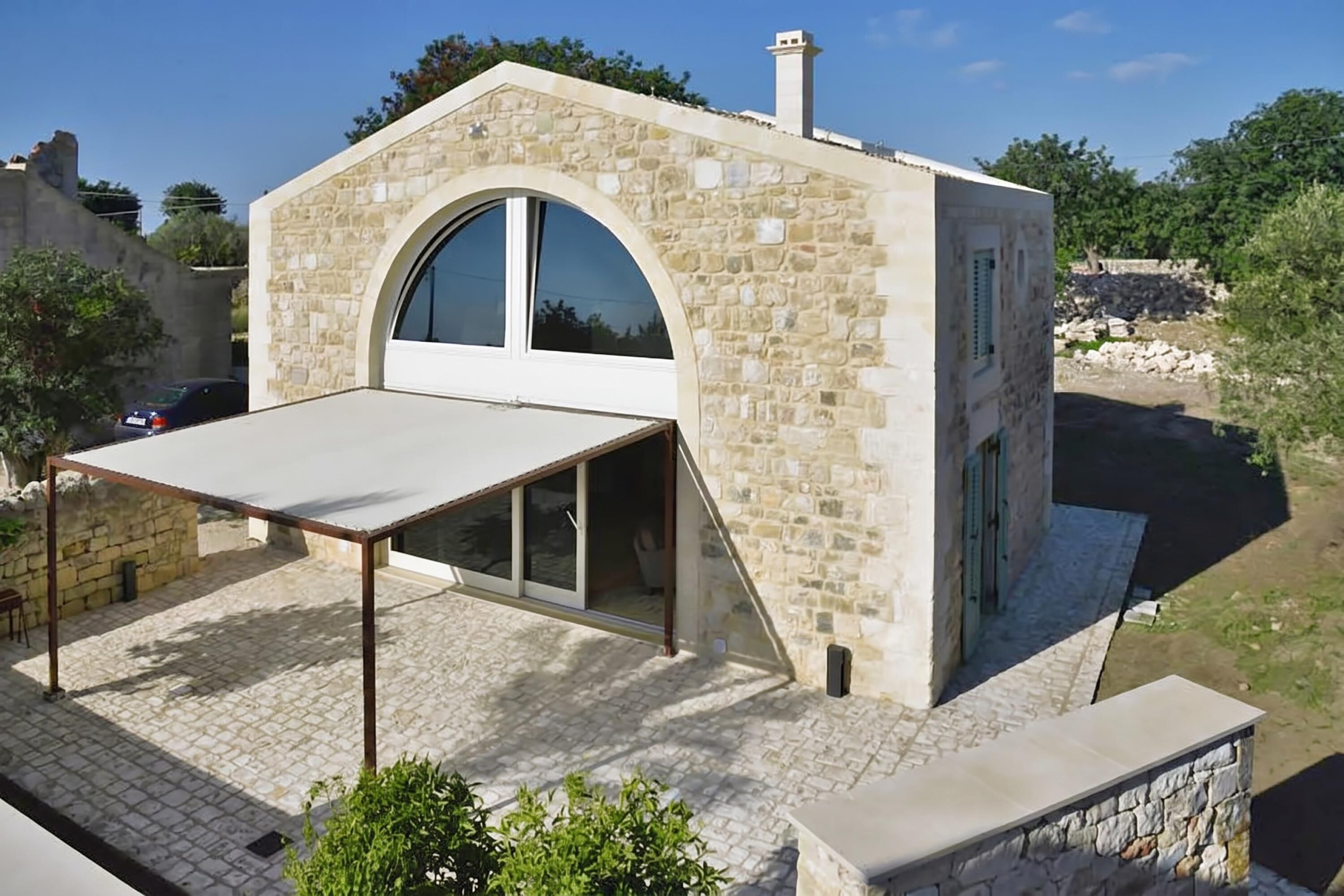 Un bâtiment en pierre doté d’une grande fenêtre en arc de cercle, d’un patio couvert et d’un mur en pierre.