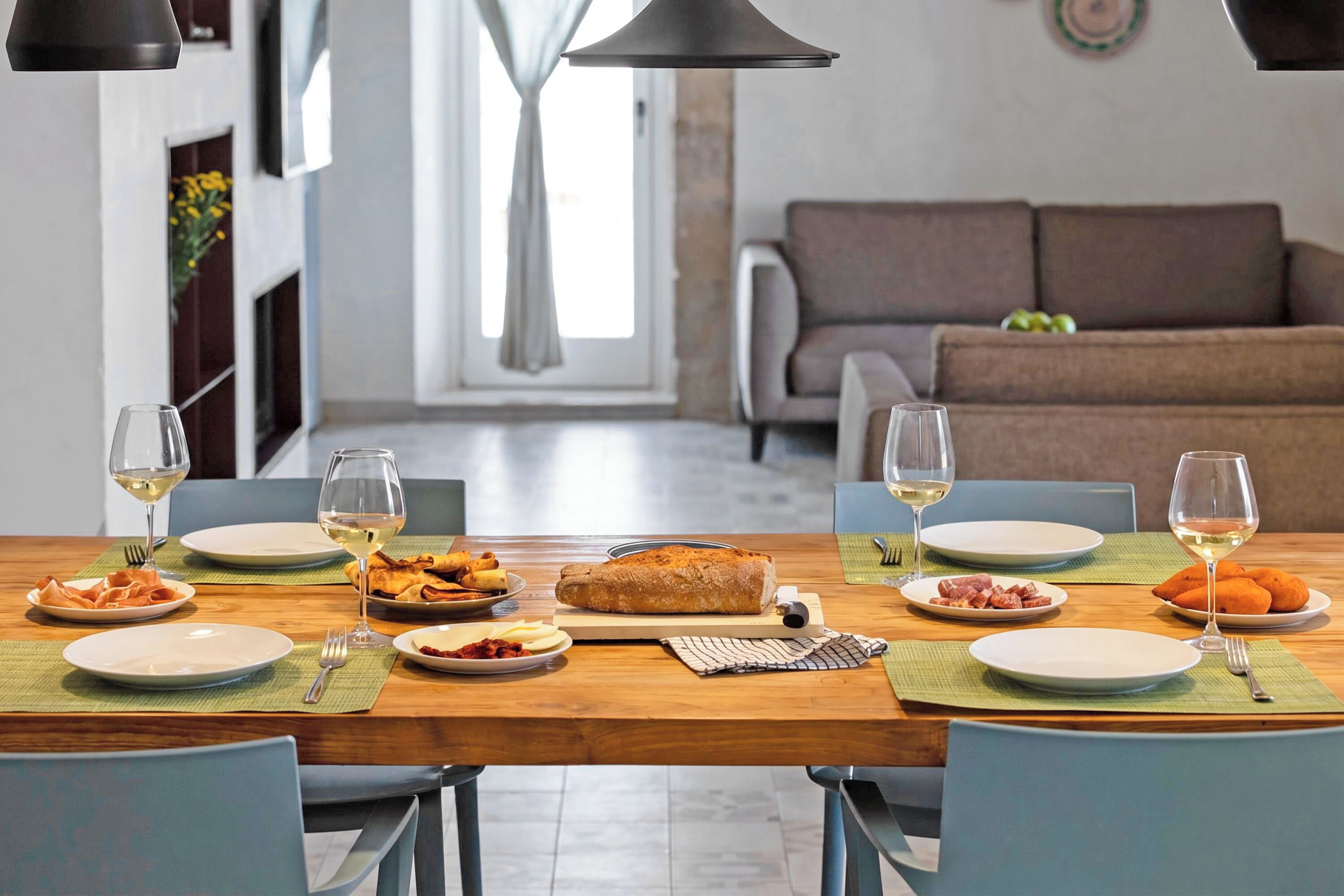 Een eettafel gedekt met borden, glazen en eten, met een bank en gordijnen op de achtergrond.