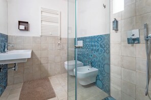 Une salle de bain avec une douche à parois de verre, un lavabo blanc, un bidet et des toilettes.