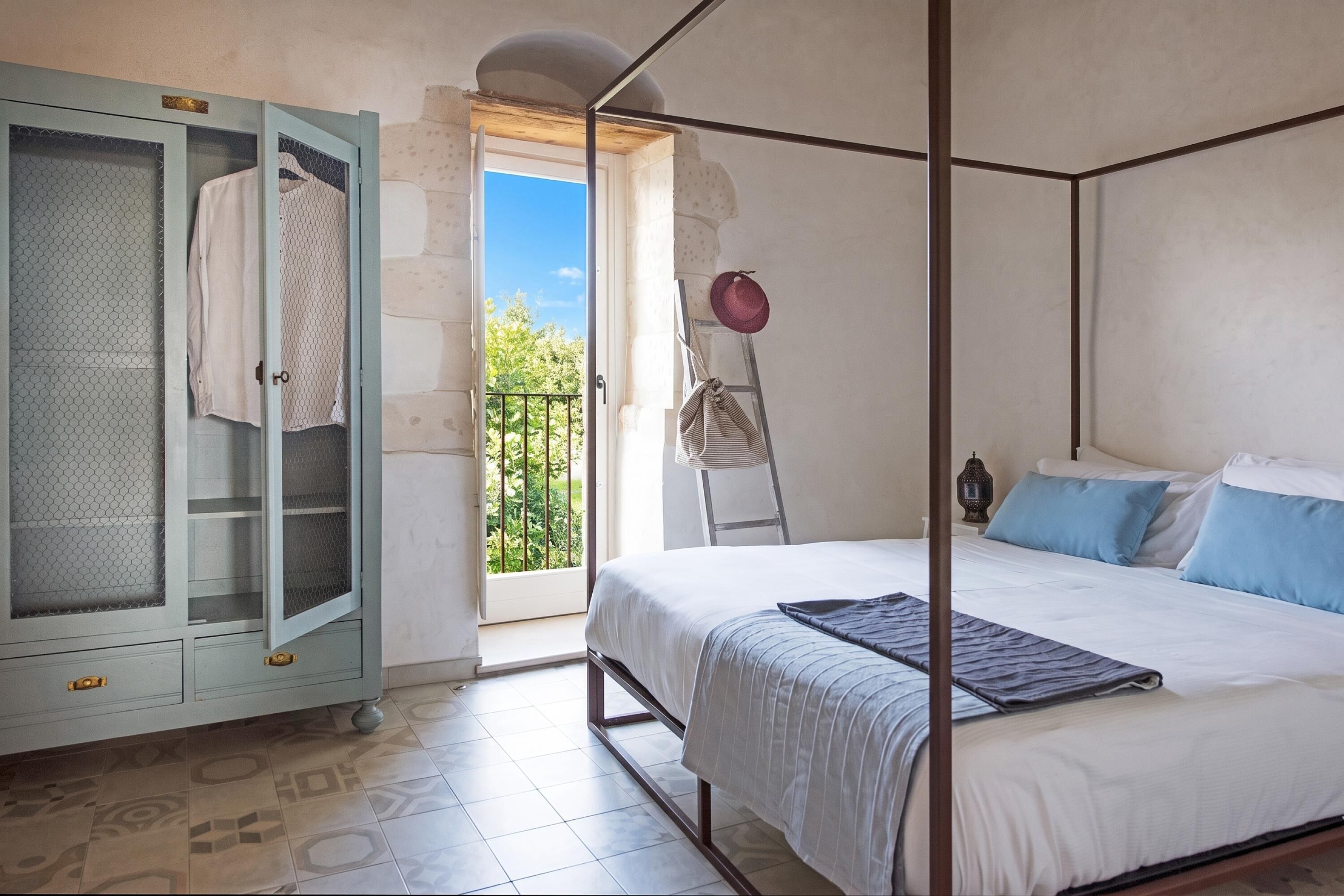 Un dormitorio con cama con dosel, armario con puerta de malla y balcón con vistas.