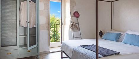 Un dormitorio con cama con dosel, armario con puerta de malla y balcón con vistas.