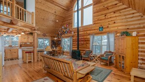 A log cabin interior with a dining area, kitchen, and a large window. - Log Cabin Hideaway- Cozy Mountain Getaway (Arnold)