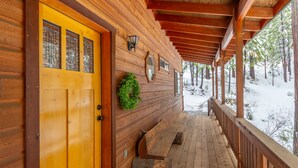 Een houten hut met een overdekte veranda, een gele deur en een kleine groene krans.