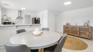 A modern kitchen with white cabinets, a built-in oven, and a dining area with a round table and chairs. - Albatross-96 Albatross Ave Hayborough (Hayborough)