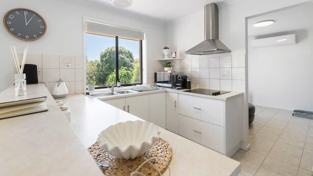 A modern kitchen with white cabinetry, a large island, a built-in stove, and a window providing a view of greenery. - Albatross-96 Albatross Ave Hayborough (Hayborough)
