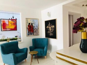 Una sala de estar moderna con sillones color turquesa, una pequeña mesa redonda y obras de arte en las paredes.