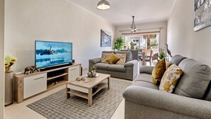 A modern living room with a flat-screen TV, a sofa, a coffee table, and a dining area in the background.