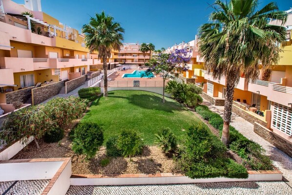 A courtyard with a swimming pool, palm trees, and a well-maintained lawn.