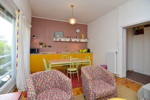 Eine kompakte Küche mit Essbereich, ausgestattet mit einem kleinen Tisch und zwei gemusterten Stühlen, einer Pendelleuchte und einem Fenster mit Vorhängen.
