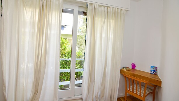 Ein Zimmer mit einem Holztisch, einem Stuhl und einem Fenster mit weißen Vorhängen.