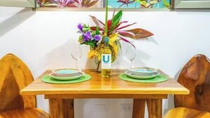 Une table de salle à manger en bois, accompagnée de deux chaises, d’un vase rempli de fleurs et d’une bouteille d’huile ULM.