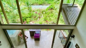 A room with a large sliding glass door leading to a balcony with a view of a lush garden and a stream. - A Sloth Riverfront Villa with Jacuzzi Pool (Bahía Ballena)
