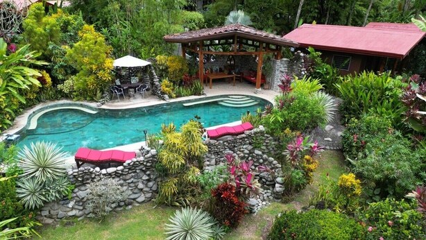 A swimming pool surrounded by lush greenery, a gazebo, and a stone wall. - A Sloth Riverfront Villa with Jacuzzi Pool (Bahía Ballena)