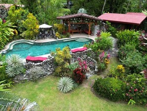 Una piscina rodeada de exuberante vegetación, un pabellón y un muro de piedra.
