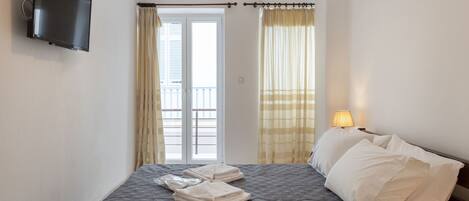 A hotel room with a bed, a TV mounted on the wall, a window with curtains, and a bedside lamp.