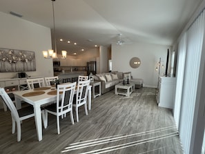 A modern living room with a dining area, a kitchen in the background, and a large window providing natural light. - CALL TODAY FOR WINTER RATES! 2/2 Gem in Village of Richmond! (The Villages)