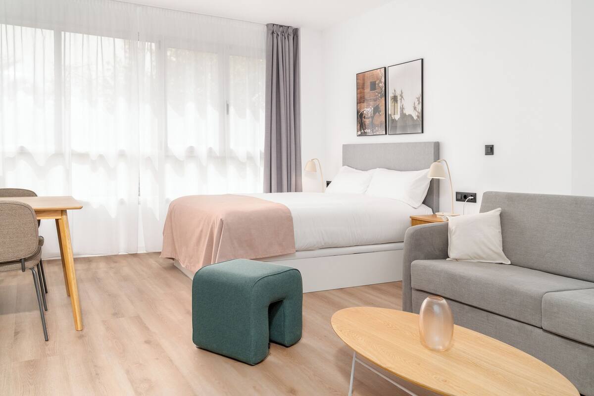 A modern hotel room with a bed, a sofa, a small table, and a chair.