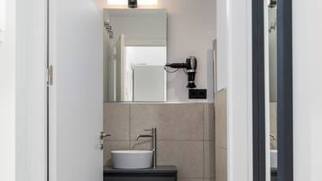 Een moderne badkamer met een witte wasbak, een spiegel en een haardroger aan de muur.