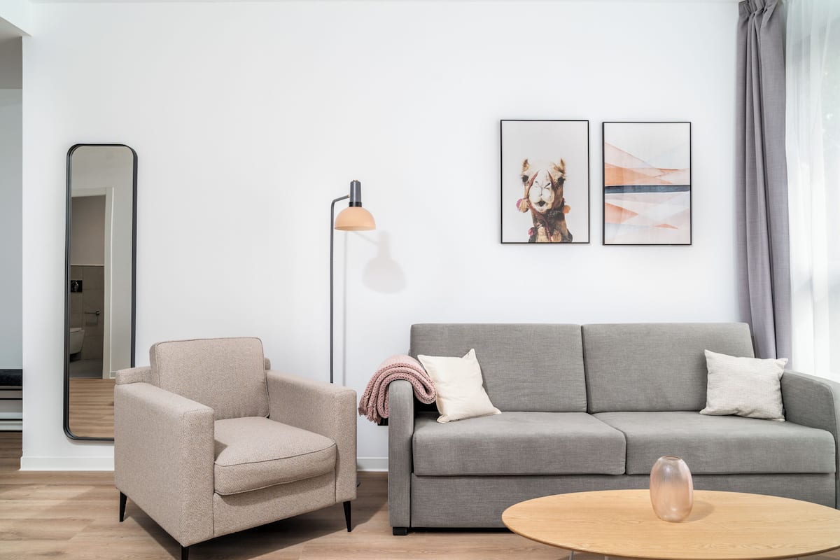 A modern living room with a grey sofa, a beige armchair, a floor lamp, and two framed artworks on the wall.