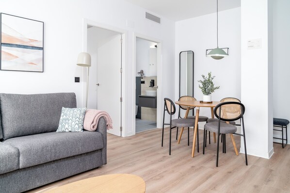 A modern living room with a grey sofa, a dining table with chairs, and a small round table. - Limehome Valencia Carrer d’Antonio Ferrandis (Valencia)
