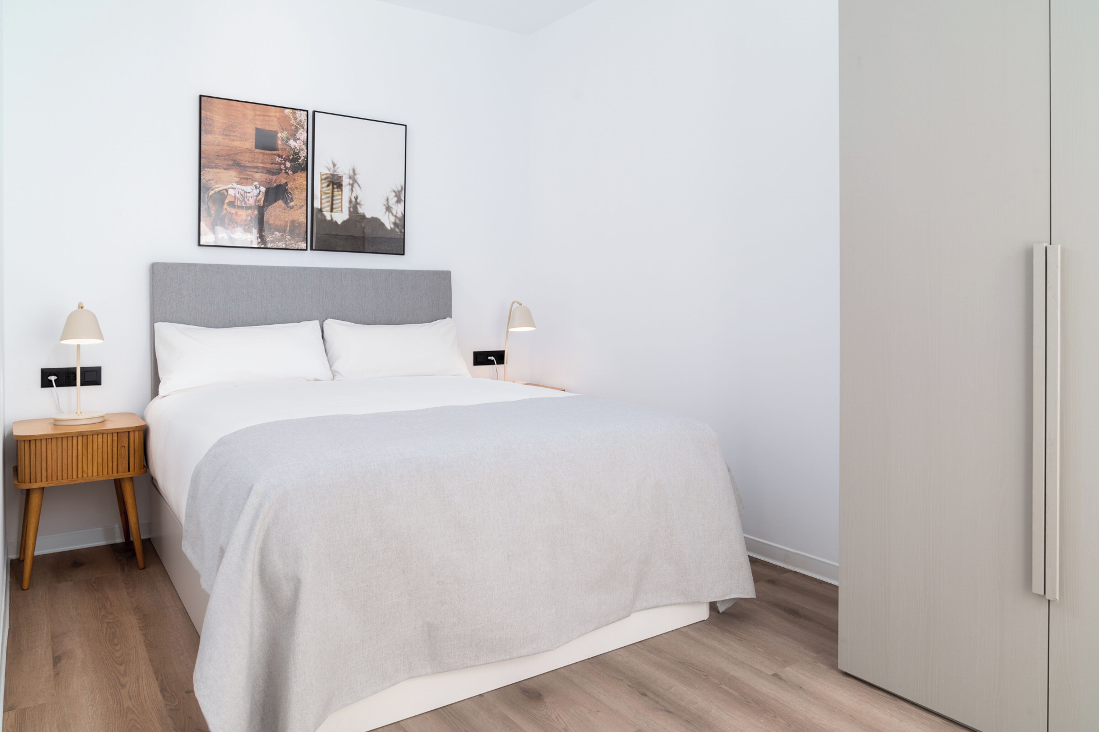 A modern bedroom with a bed, two bedside tables, a wardrobe, and two wall-mounted pictures.