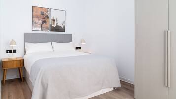 A modern bedroom with a bed, two bedside tables, a wardrobe, and two wall-mounted pictures.