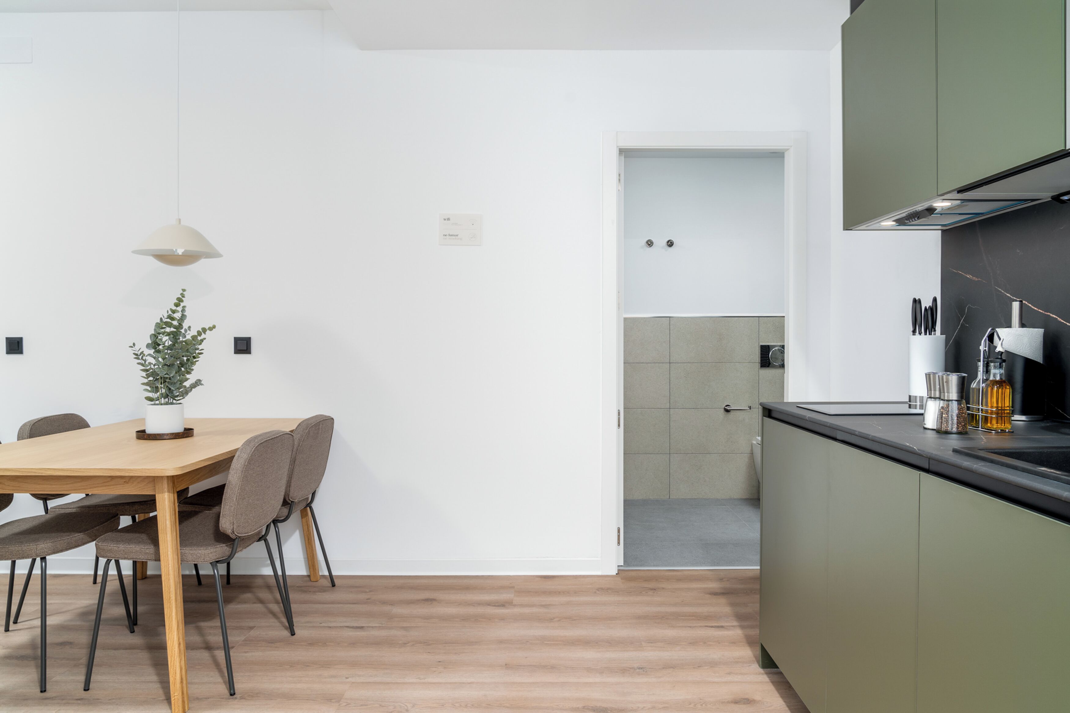 Una cocina moderna con una mesa y sillas de madera, una planta en maceta, y vistas a la habitación contigua.