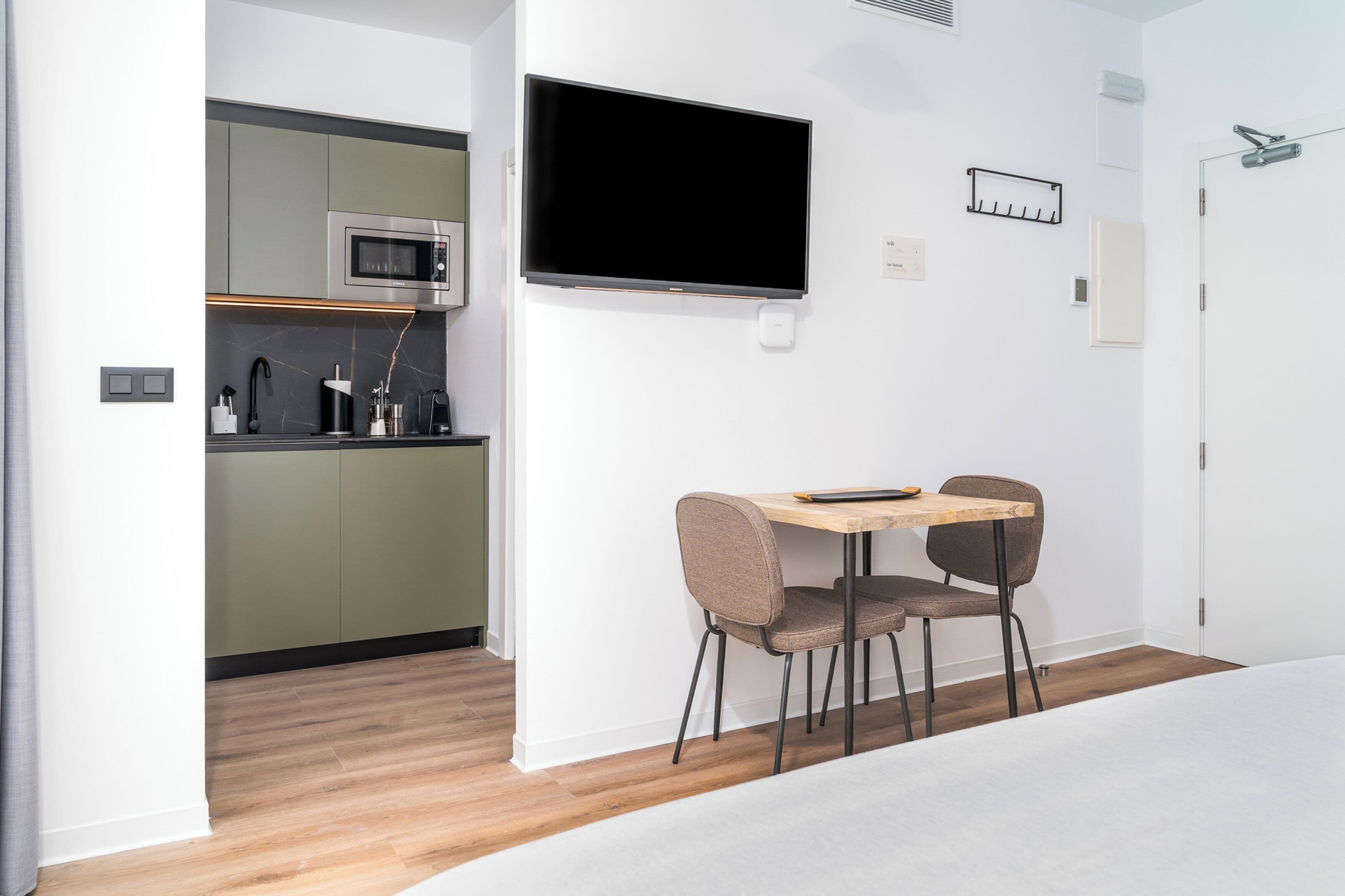 Una cocina moderna con microondas, un televisor de pantalla plana montado en la pared y un comedor con mesa y dos sillas.