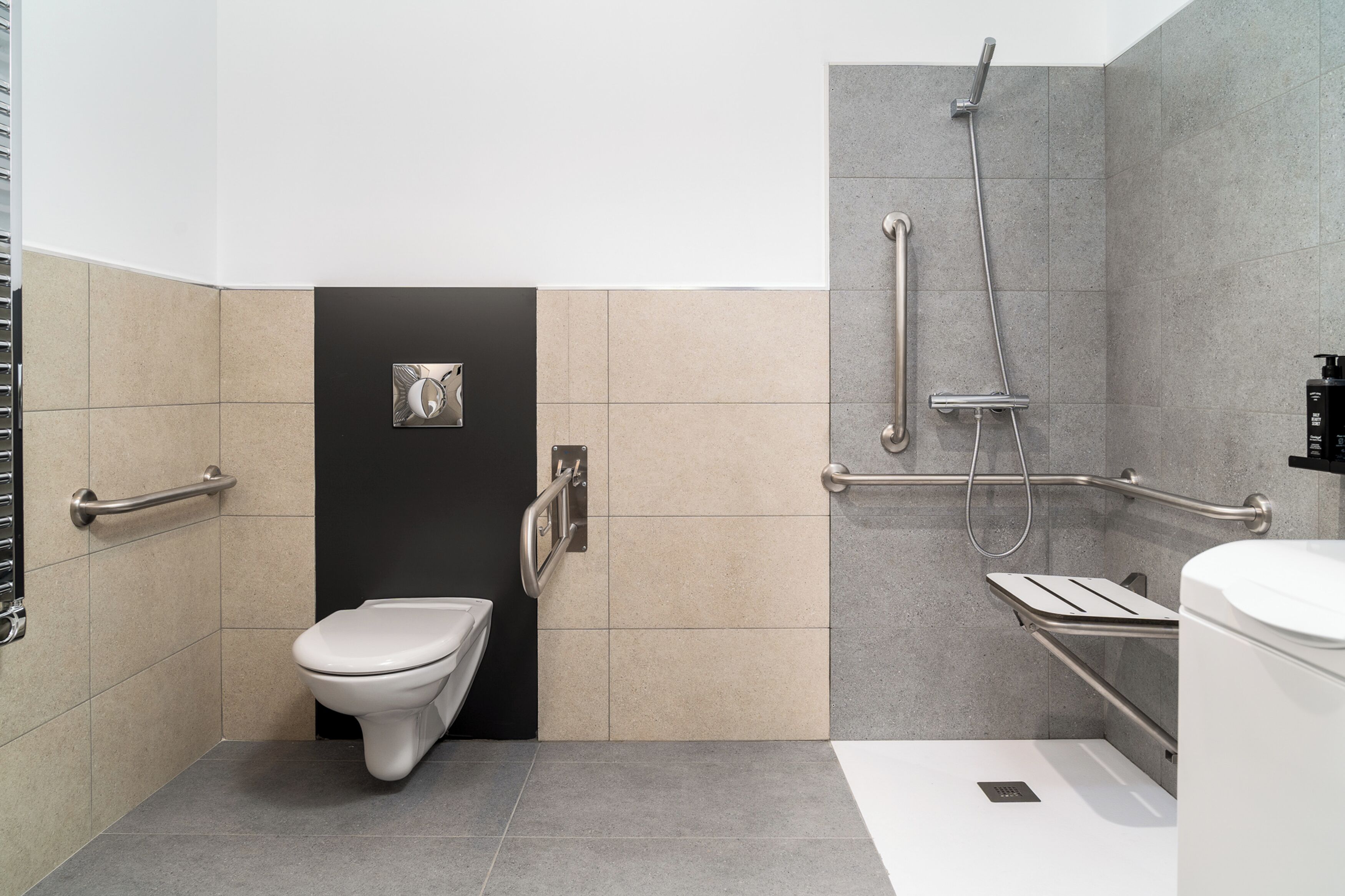 Un baño moderno con inodoro, ducha con barras de apoyo y secador de manos.