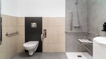 Un baño moderno con inodoro, ducha con barras de apoyo y secador de manos.
