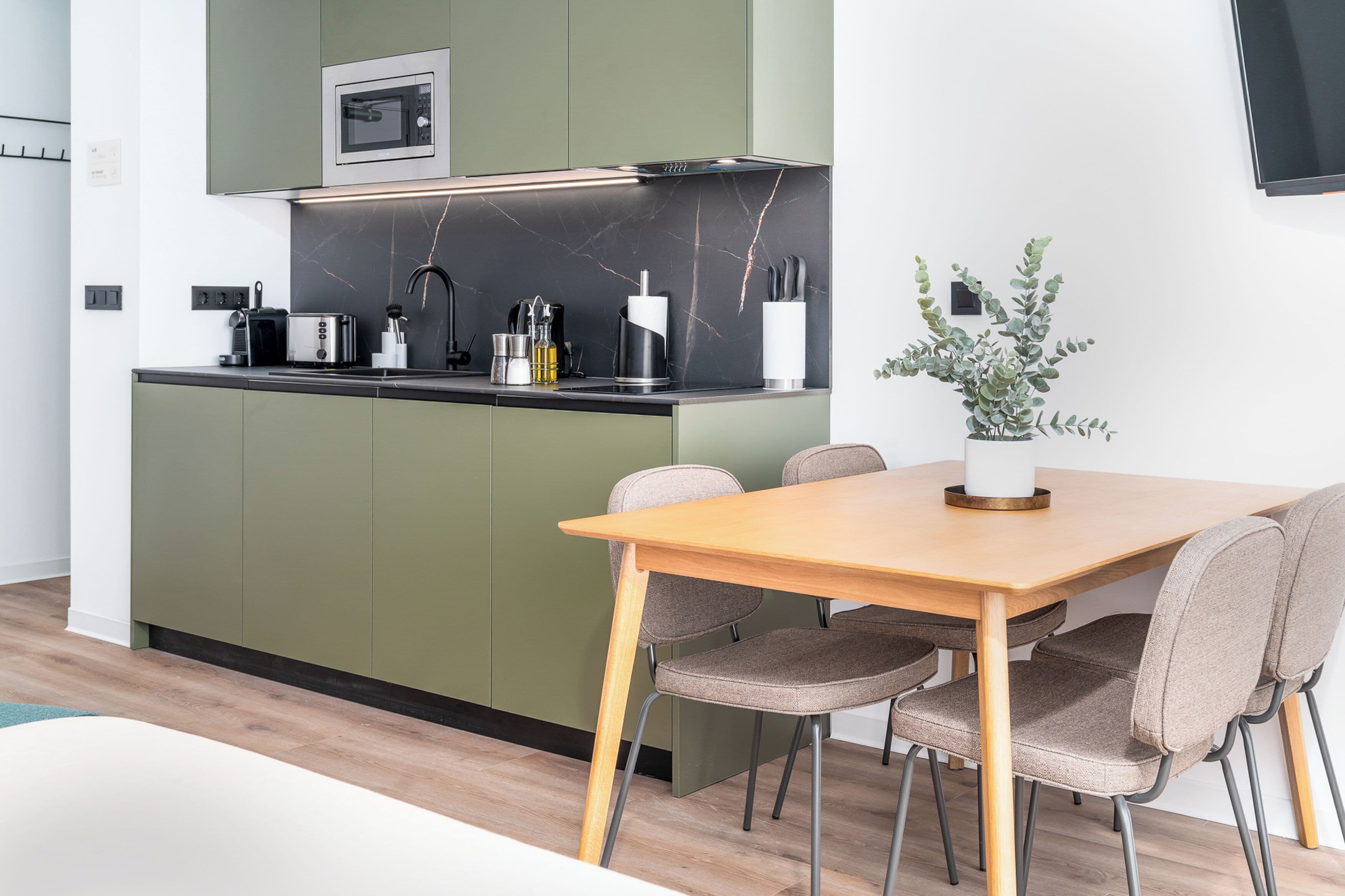 Una cocina moderna con gabinetes verdes, un microondas y un comedor con una mesa de madera y cuatro sillas.