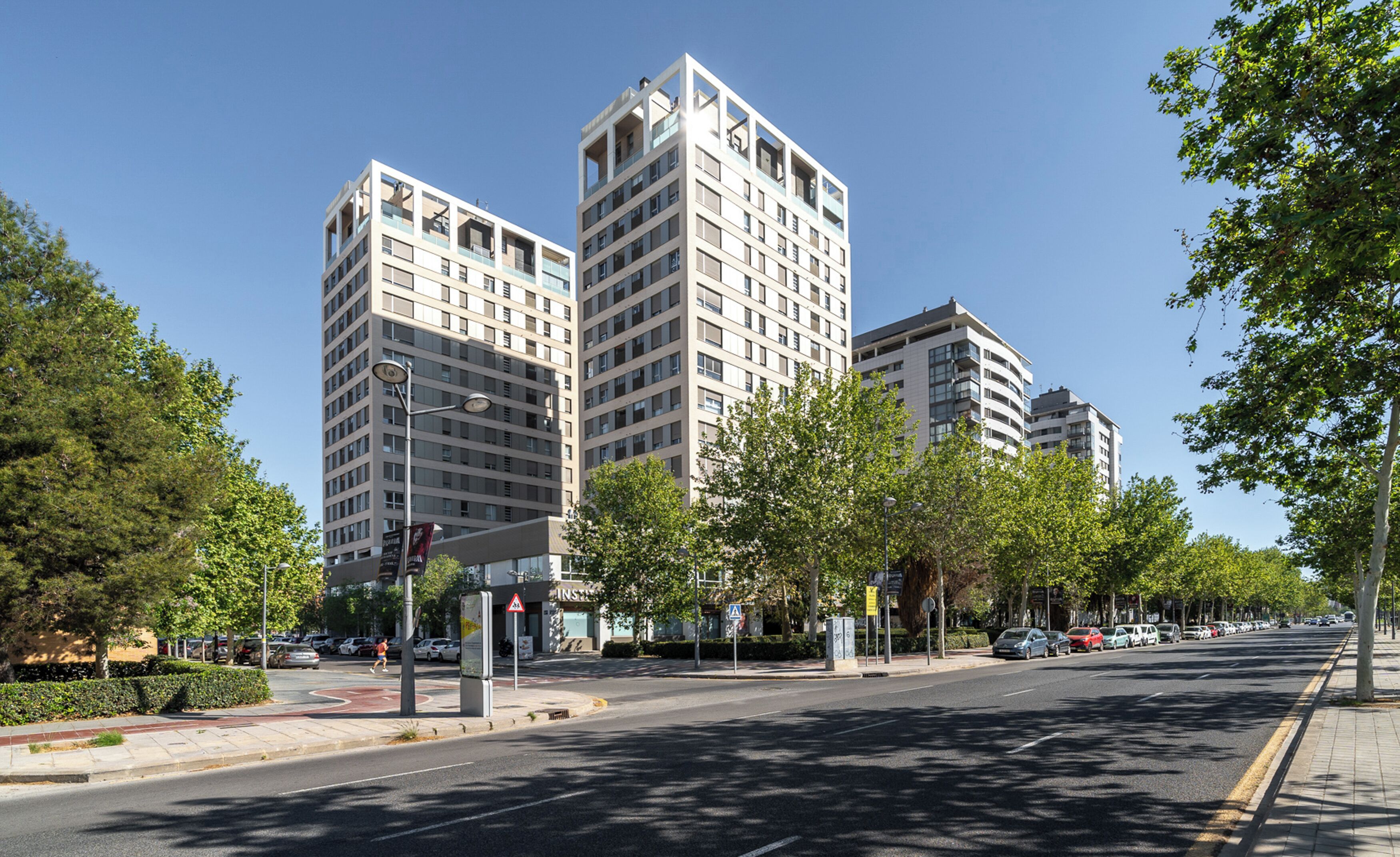 A modern urban street with high-rise buildings, a pedestrian crossing, and parked cars.