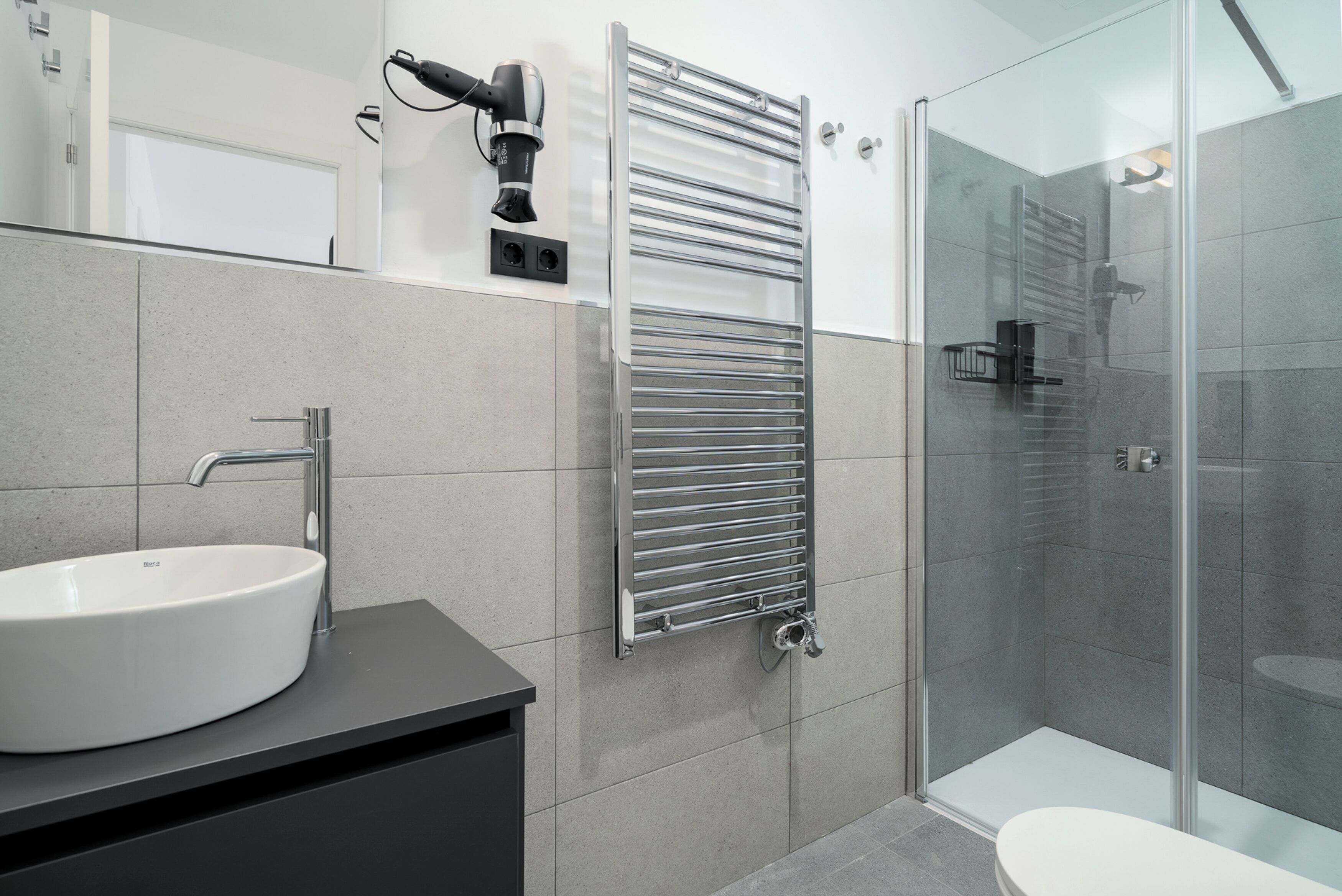 Un baño moderno con un lavamanos blanco, una cabina de ducha de vidrio y un perchero para toallas.