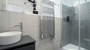Un baño moderno con un lavamanos blanco, una cabina de ducha de vidrio y un perchero para toallas.
