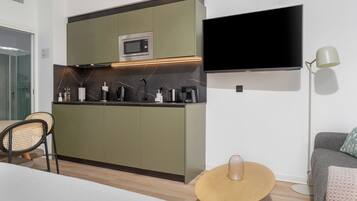 A compact kitchen with a microwave, a flat-screen TV, and a dining area with a round table and chairs.