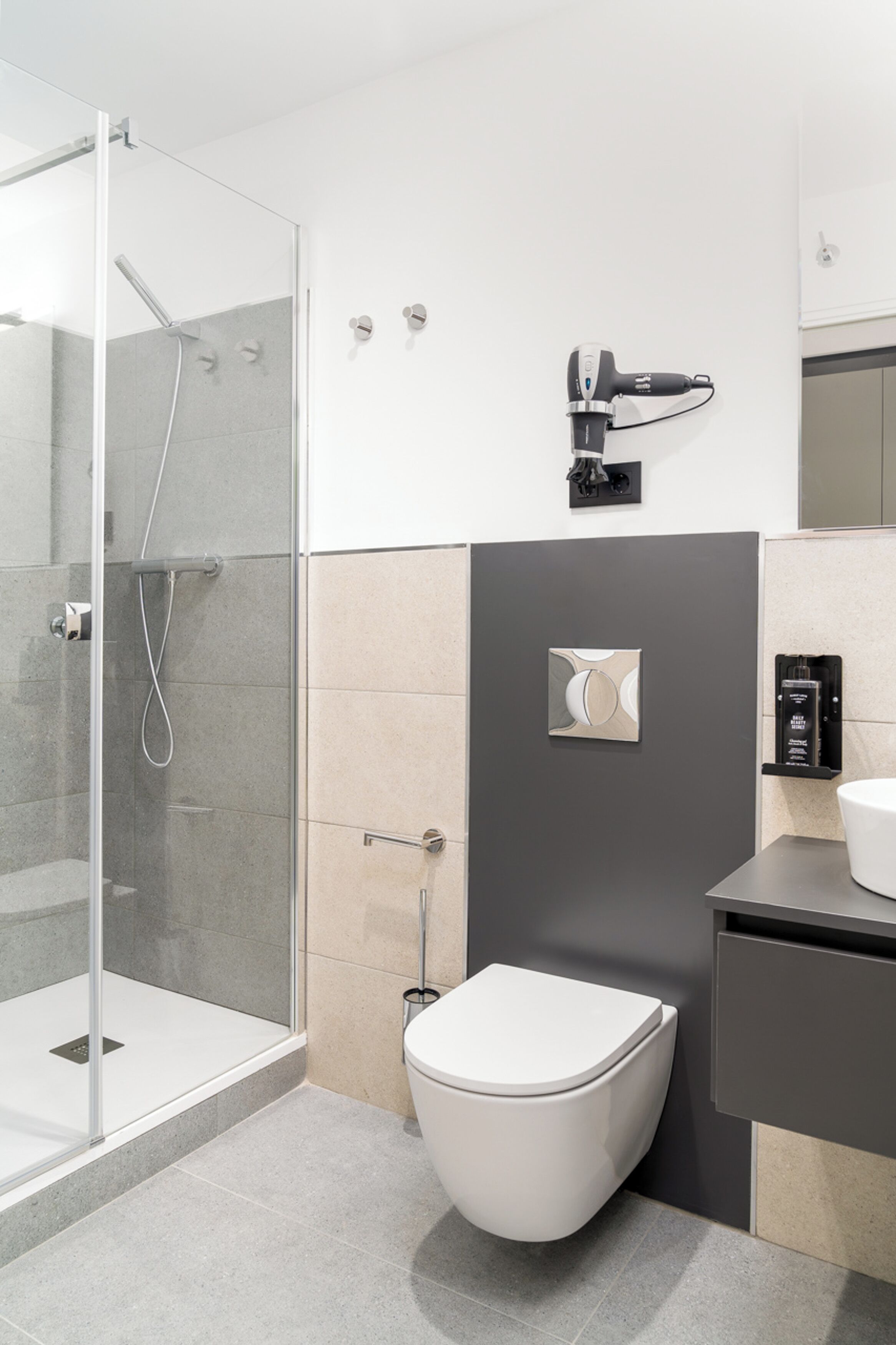 A modern bathroom with a glass-enclosed shower, a toilet, and a hairdryer mounted on the wall.