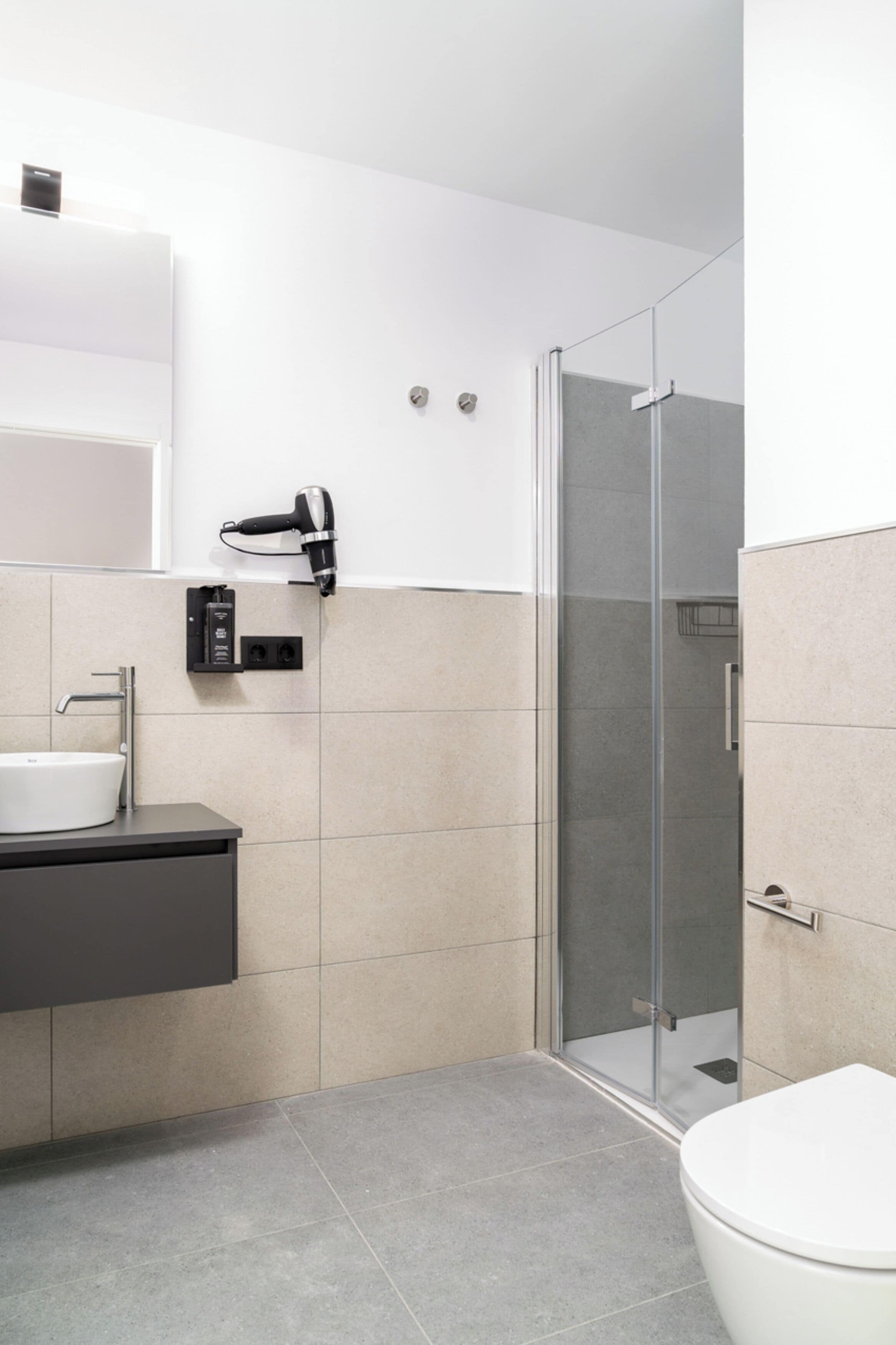 A modern bathroom with a glass shower enclosure, a white sink, and a toilet.