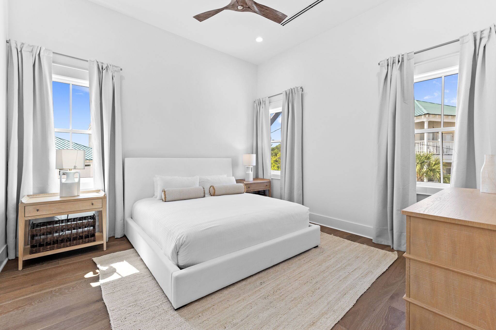 A modern bedroom with a large bed, bedside tables, a nightstand, and a view of the outside.